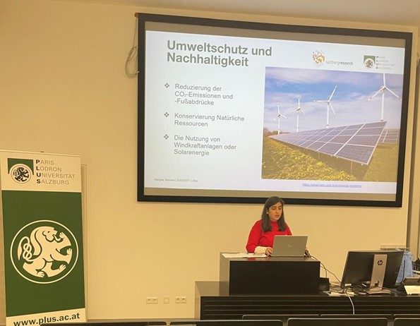 Narges Mehran steht in einem Vorlesungssaal der Universität Salzburg und präsentiert eine Folie zum Umweltschutz und der Nachhaltigkeit im Kontext der Datenverarbeitung. 