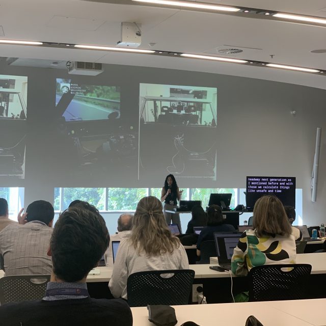 Cansu Demir presents driving simulator studies at an academic conference, with technical slides projected behind and an engaged audience in attendance.